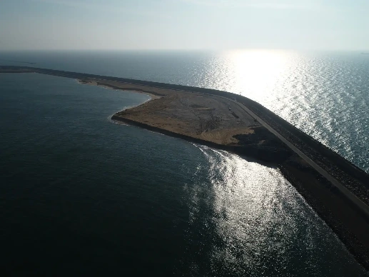 Long ocean breakwater of CWIT with land and bright horizon.