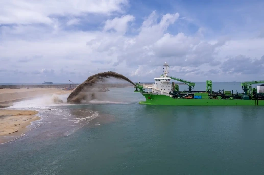 Dredging vessel spraying sand onto a shoreline under a cloudy sky.