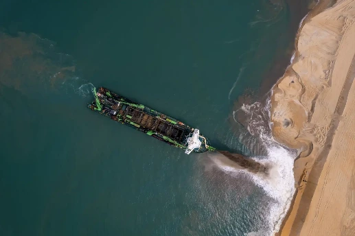 A drone shot of a dredging vessel spraying sand onto a shoreline.